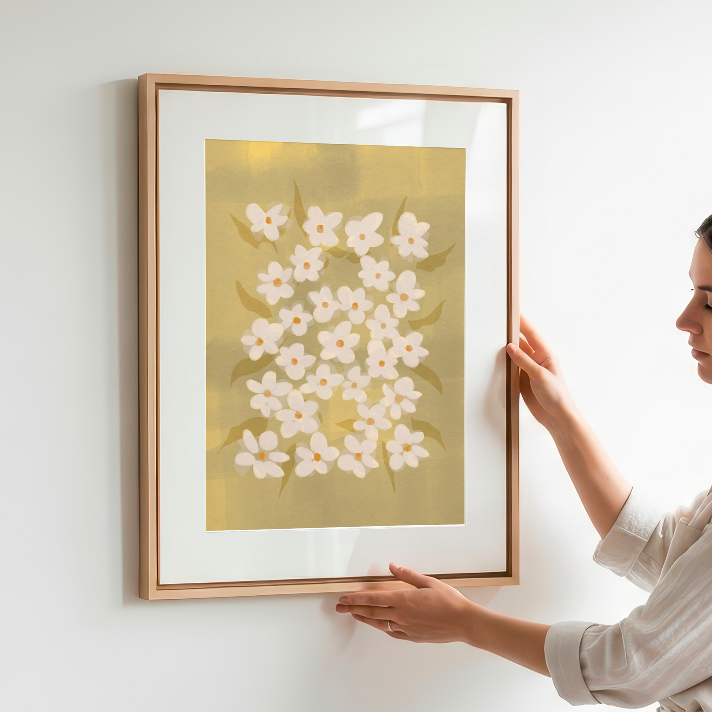 Person hanging a framed artwork of white flowers on a light wall